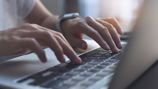 A close-up of a person typing on the keyboard of their laptop