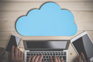 A cloud icon on a desk in front of a laptop.