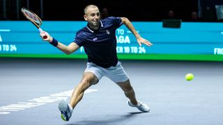 Dan Evans lunges for a forehand in the Davis Cup 2024, wearing a blue shirt and white shorts.